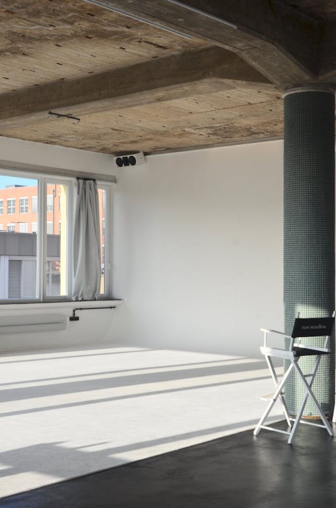 pexels-photo-6045329 Spacious modern loft with natural light and minimalist design featuring a white chair and pillar.
